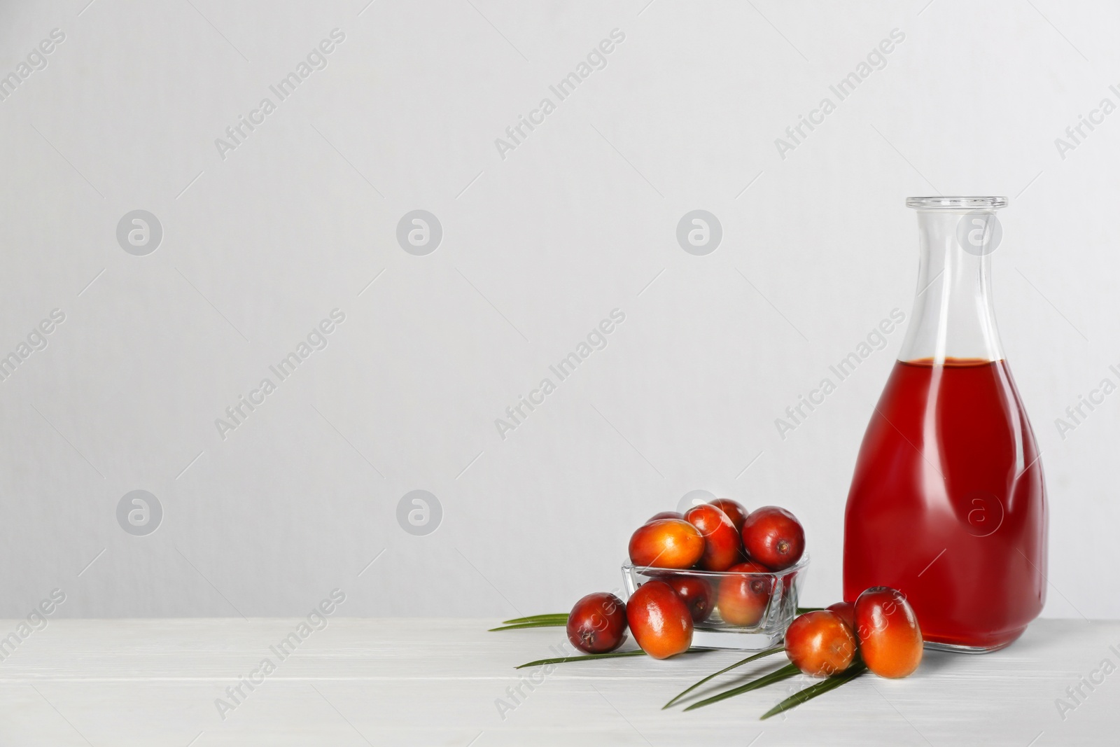 Photo of Palm oil in glass bottle, tropical leaf and fruits on white wooden table. Space for text