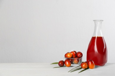 Photo of Palm oil in glass bottle, tropical leaf and fruits on white wooden table. Space for text