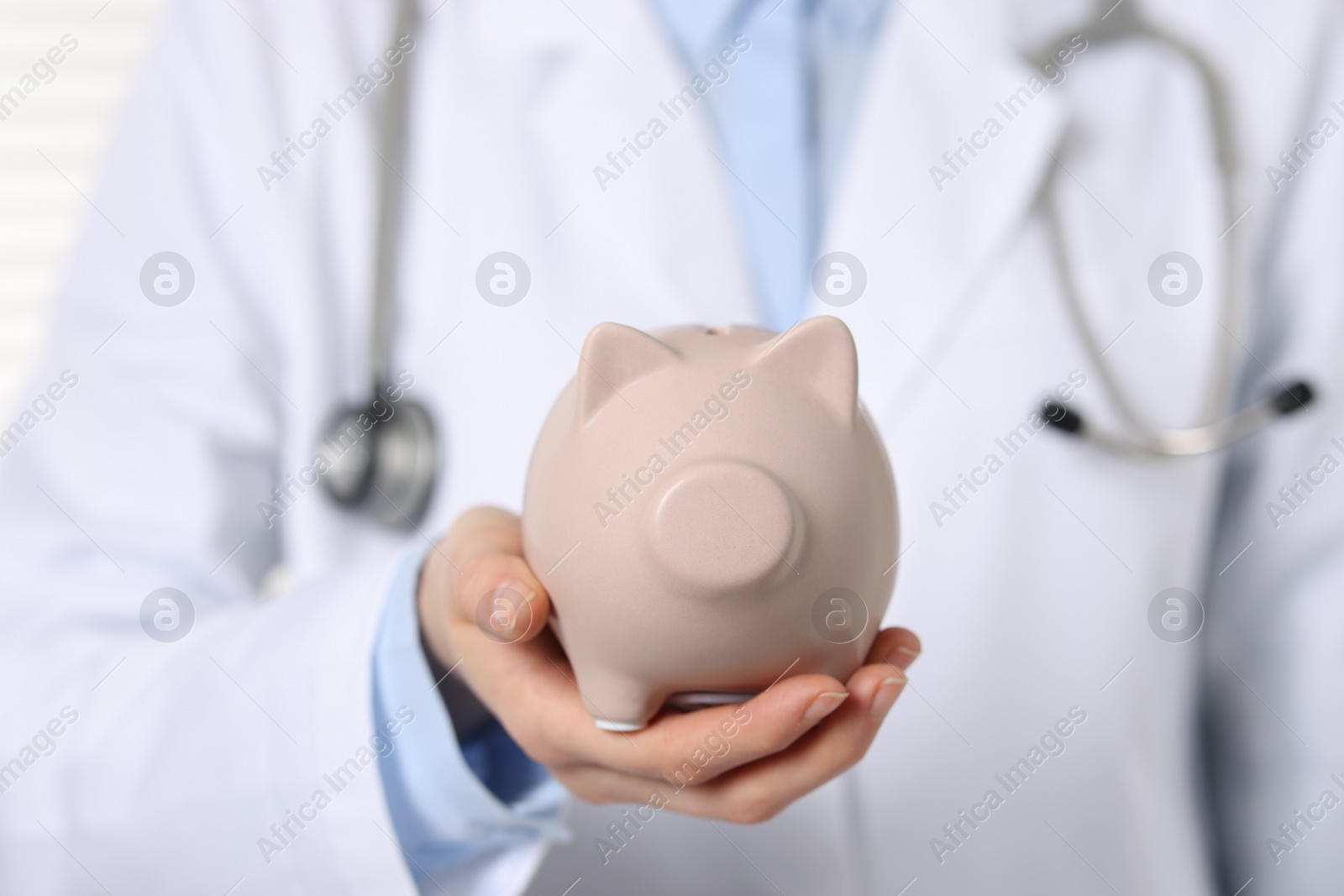 Photo of Doctor with beige ceramic piggy bank, closeup