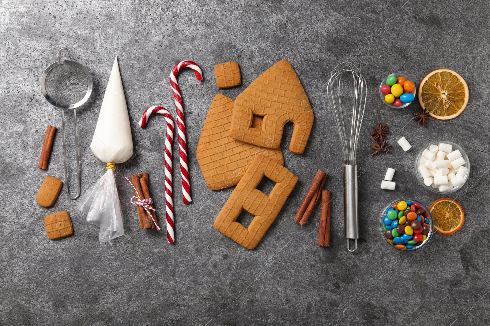 Photo of Parts of gingerbread house, kitchenware and ingredients for decoration on grey table, flat lay