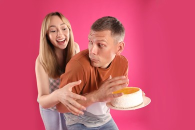 Photo of Greedy man hiding tasty cake from woman on pink background