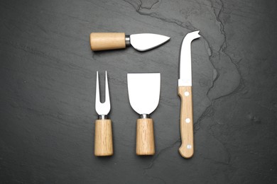 Photo of Cheese knives and fork on black stone table, flat lay