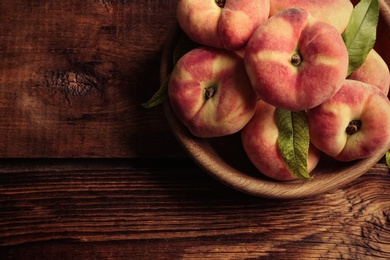 Photo of Fresh ripe donut peaches in bowl on wooden table, top view. Space for text