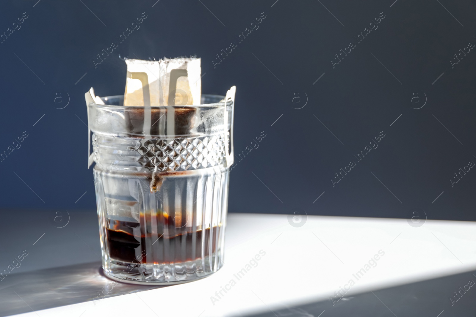 Photo of Glass with drip coffee bag on light grey table, closeup. Space for text