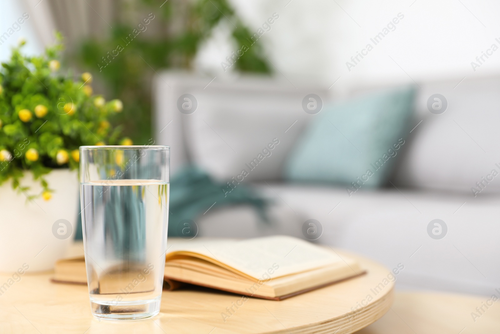 Photo of Glass of water and book on coffee table in modern living room interior. Space for text