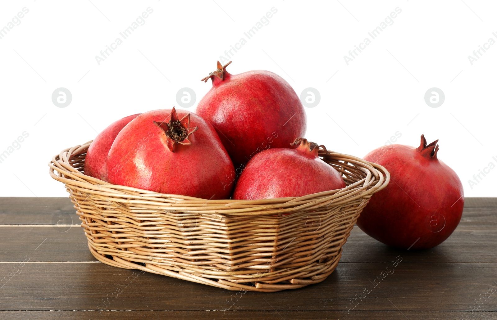 Photo of Fresh pomegranates in wicker basket on wooden table against white background