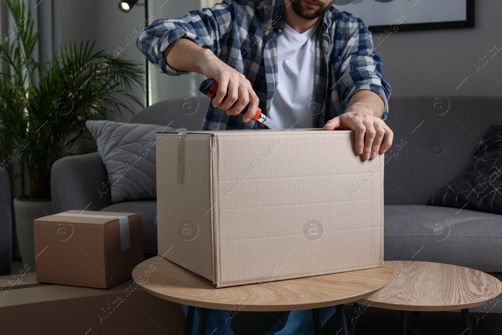 Photo of Man using utility knife to open parcel at home, closeup