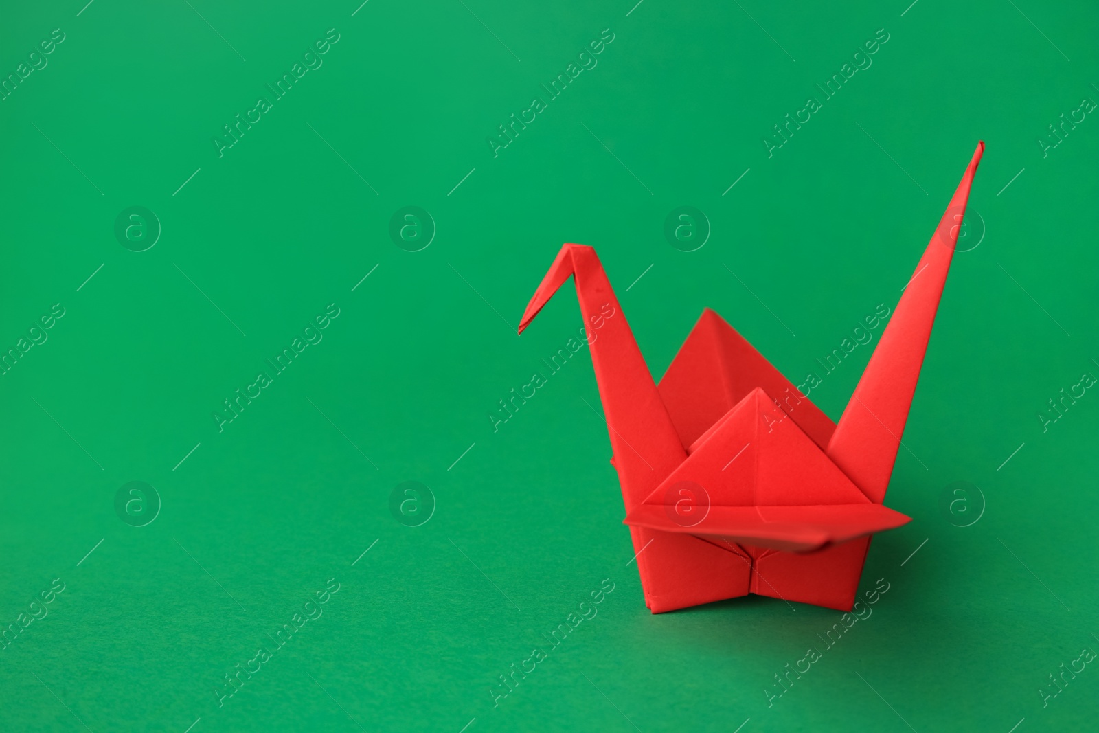 Photo of Red paper origami crane on green background, space for text