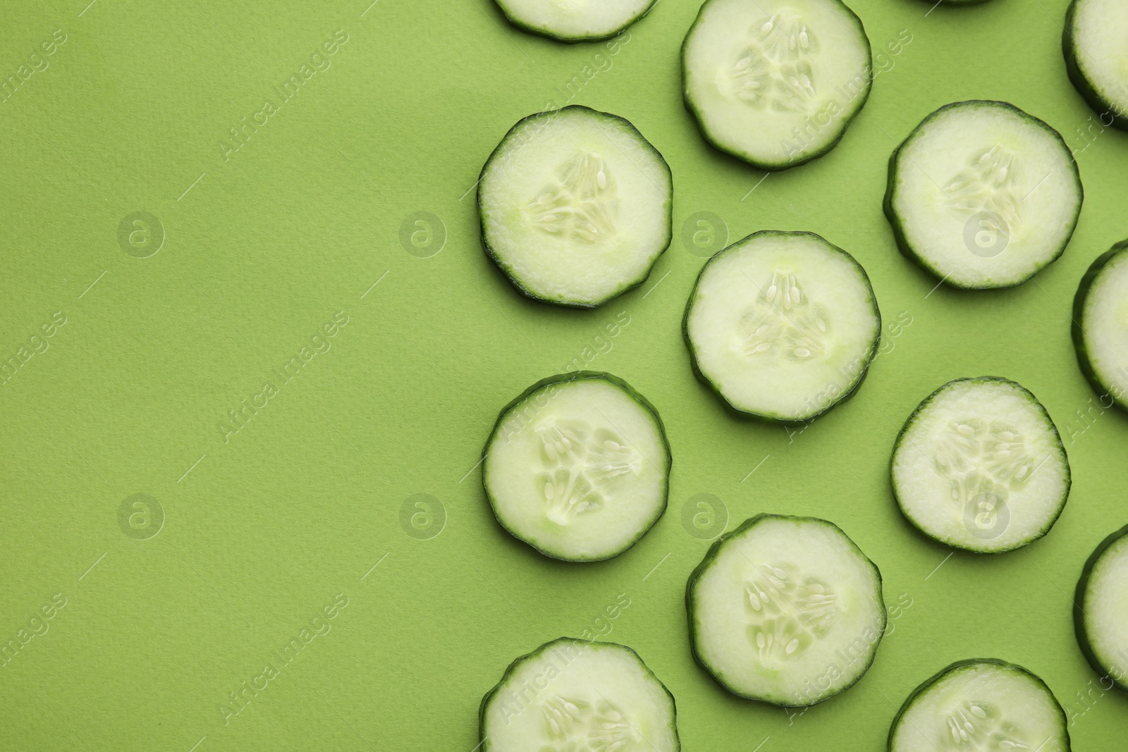 Photo of Fresh slices of cucumbers on green background, top view. Space for text