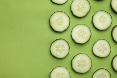 Fresh slices of cucumbers on green background, top view. Space for text