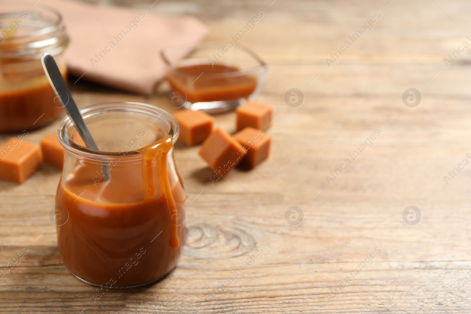 Photo of Tasty salted caramel and spoon in glass jar on wooden table, space for text