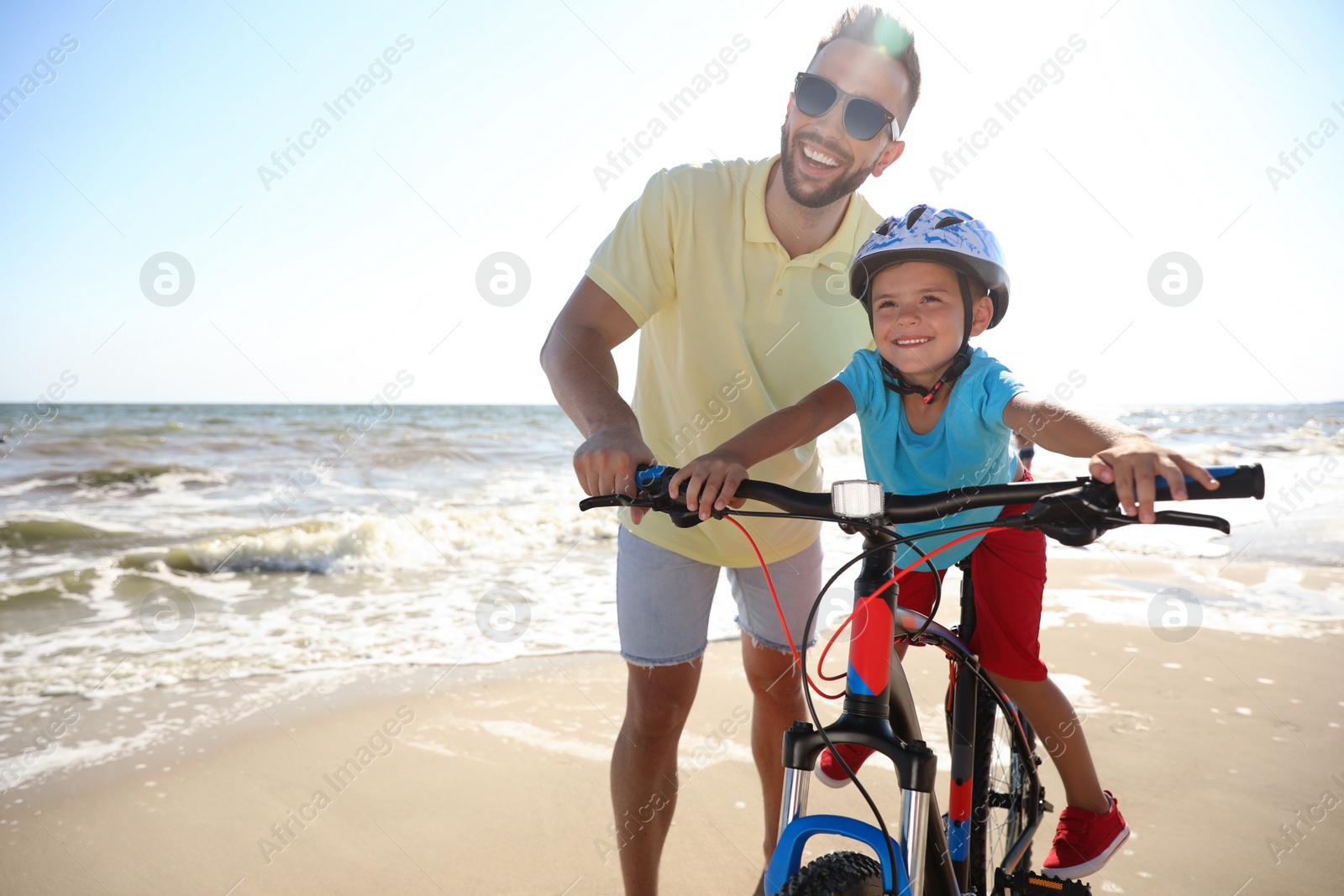 Photo of Happy father teaching son to ride bicycle on sandy beach near sea