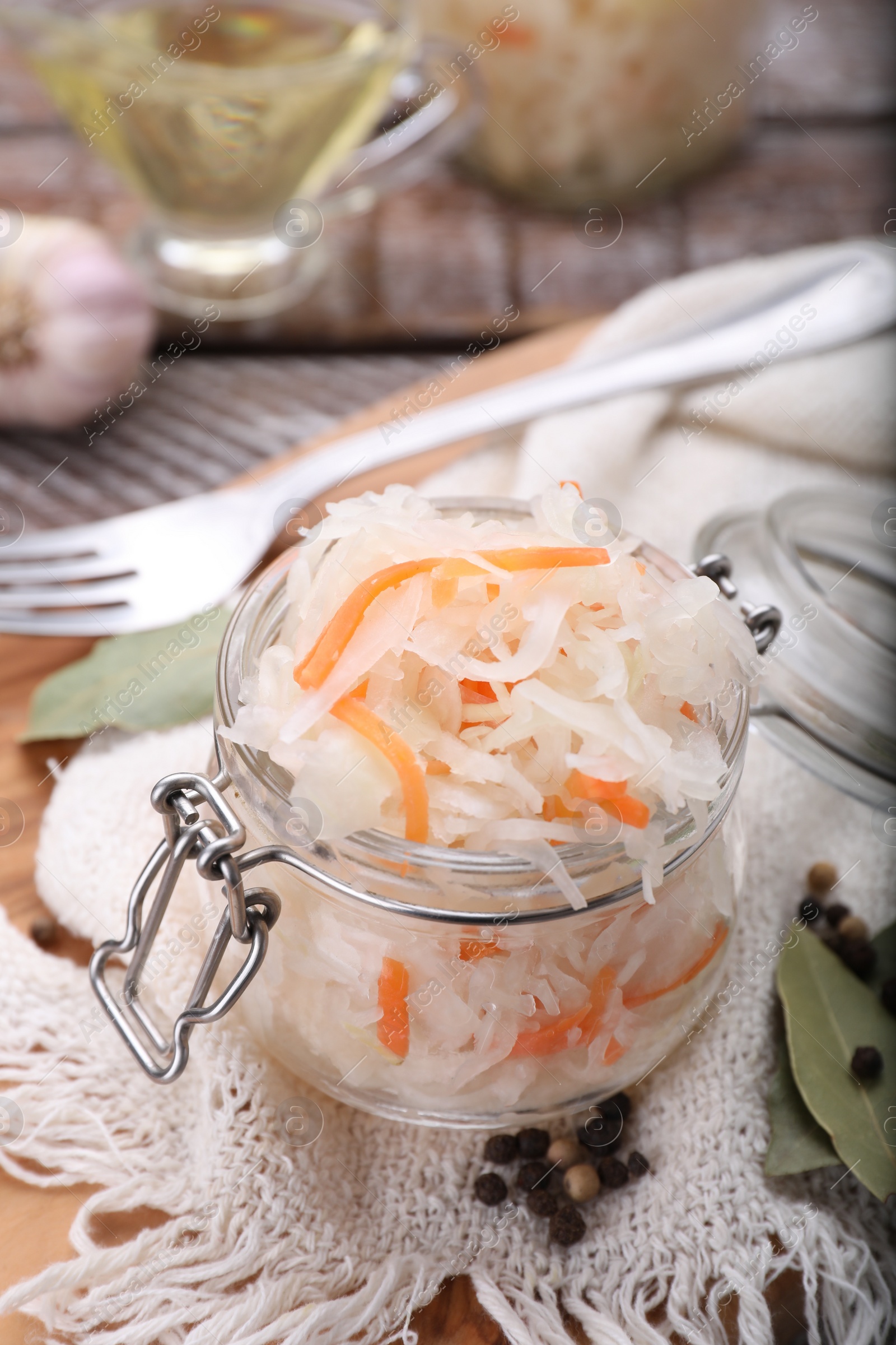 Photo of Glass jar of tasty sauerkraut and ingredients on wooden table