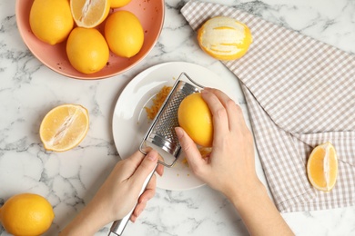 Photo of Woman zesting lemon at white marble table, top view