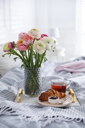Photo of Bouquet of beautiful ranunculuses, croissant and tea on bed indoors