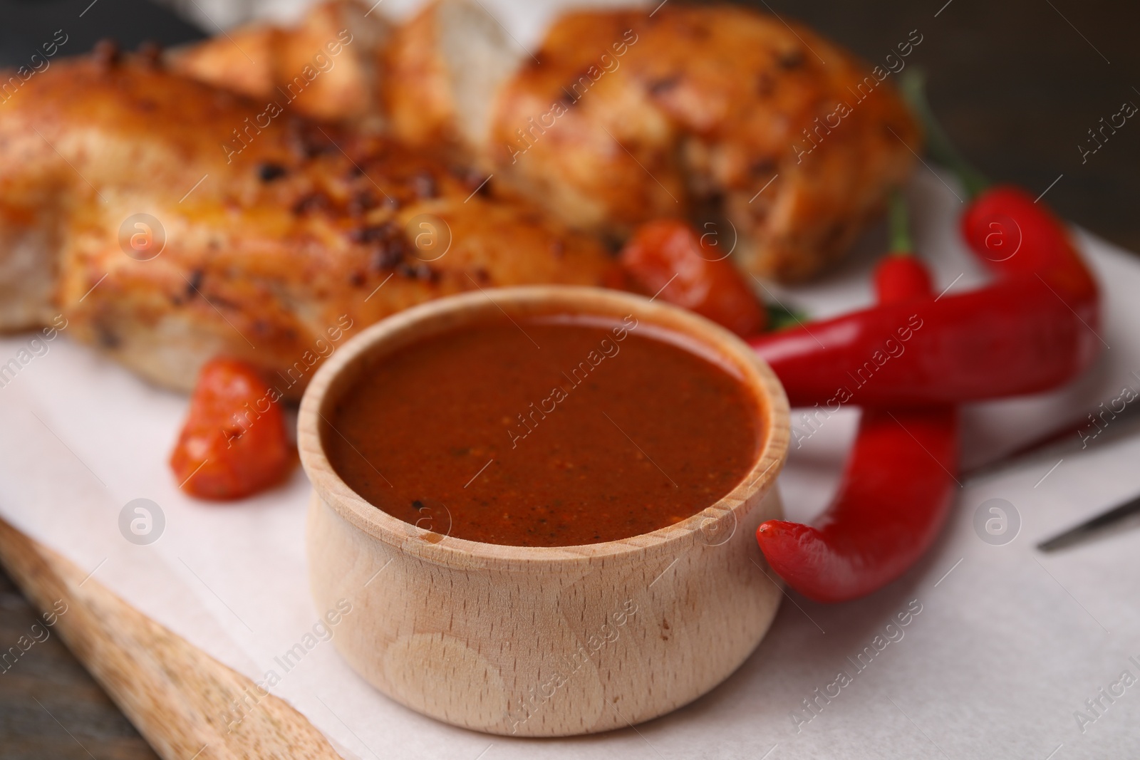 Photo of Baked chicken fillets and marinade on wooden table, closeup