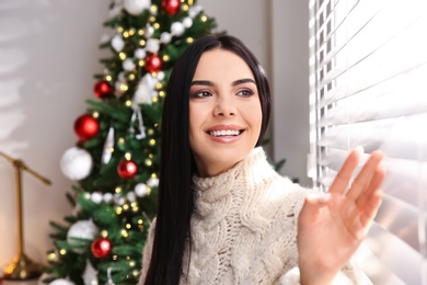 Young woman near window in room with Christmas tree