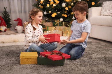 Photo of Cute little children with gift boxes near Christmas tree at home