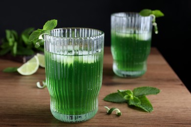 Photo of Delicious mint liqueur with green leaves and ice cubes on wooden table