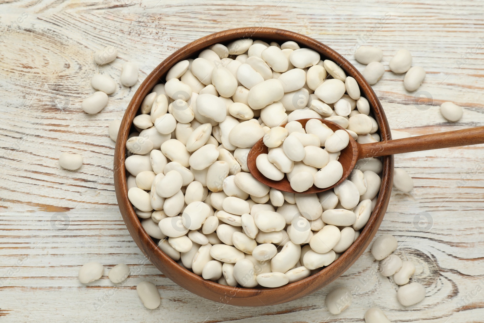 Photo of Bowl and spoon with uncooked white beans on wooden table, flat lay