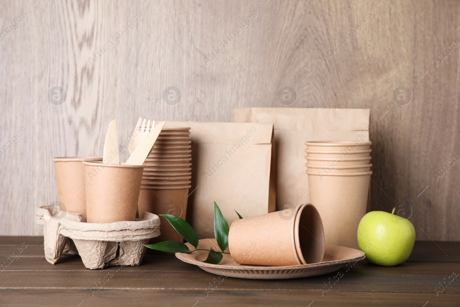 Photo of Set of disposable eco friendly dishware and apple on wooden table