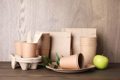 Photo of Set of disposable eco friendly dishware and apple on wooden table