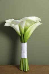 Beautiful calla lily flowers tied with ribbon on wooden table near olive wall