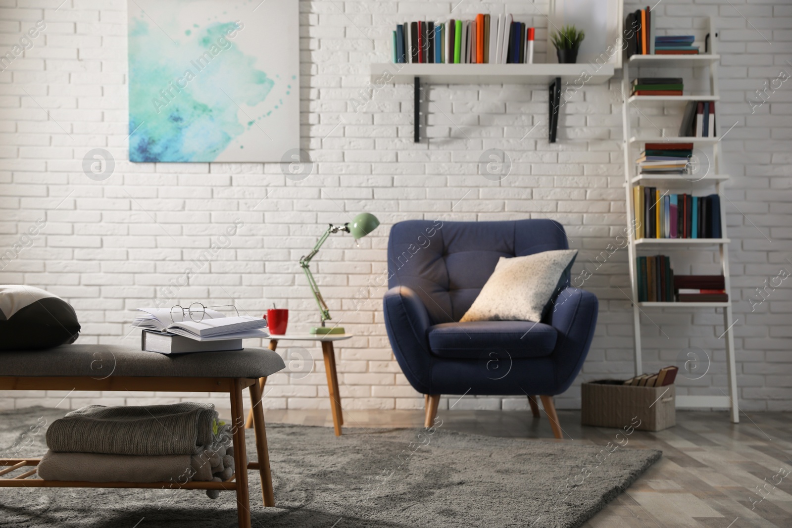 Photo of Room interior with comfortable armchair and different books near brick wall