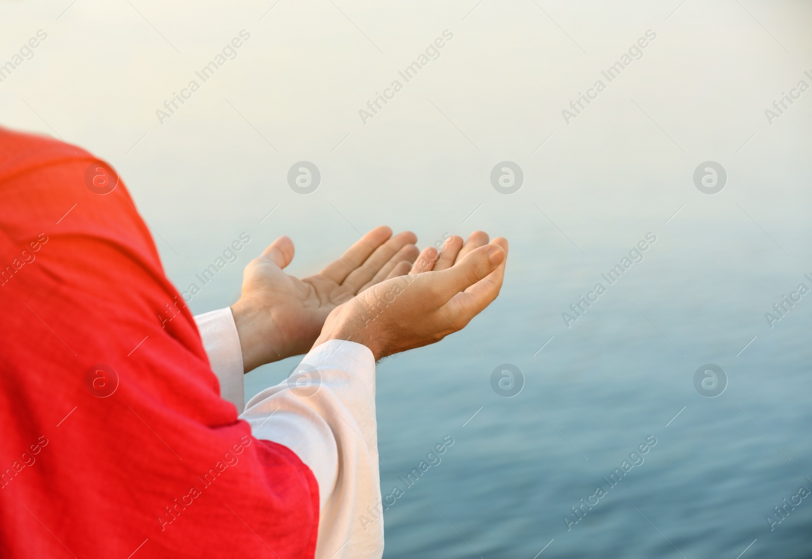 Photo of Jesus Christ reaching out his hands near water outdoors, closeup