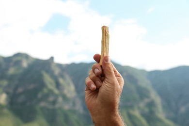 Photo of Man holding palo santo stick in high mountains, closeup