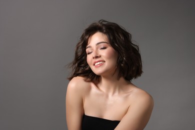 Portrait of beautiful young woman with wavy hairstyle on grey background