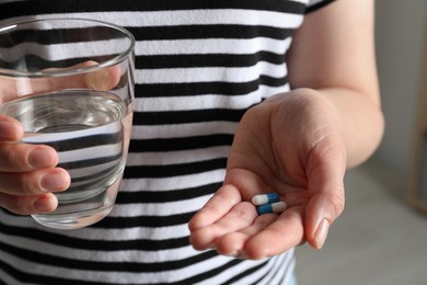 Woman with glass of water and pills on blurred background, closeup