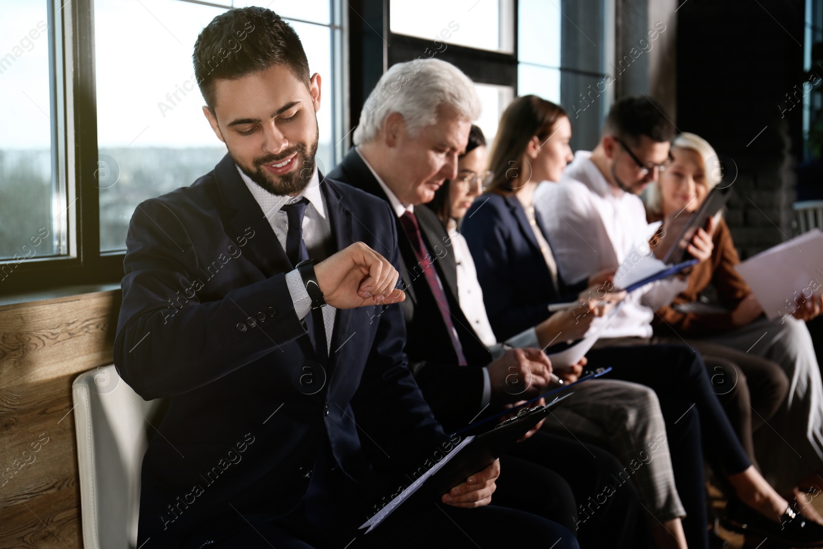 Photo of Young man checking time while waiting for job interview in office hall