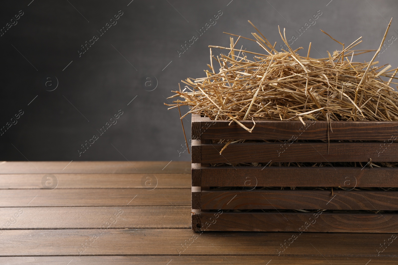 Photo of Dried straw in crate on wooden table, space for text