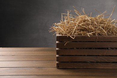 Dried straw in crate on wooden table, space for text