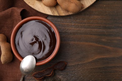 Photo of Bowl of tamarind sauce, spoon and fresh pods on wooden table, flat lay. Space for text