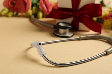 Stethoscope, gift box and flowers on beige background, closeup with space for text. Happy Doctor's Day