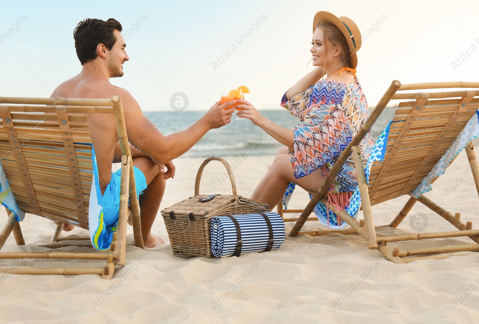 Photo of Happy young couple with cocktails sitting on deck chairs at sea beach