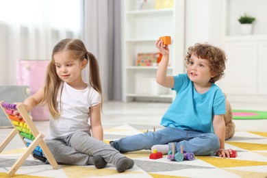Photo of Cute little children playing with different toys on floor in kindergarten