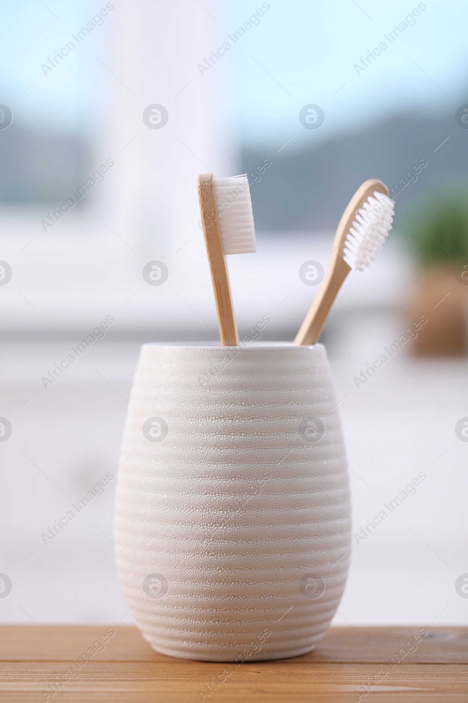 Photo of Bamboo toothbrushes in holder on wooden table