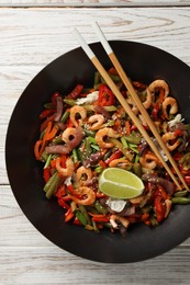 Shrimp stir fry with vegetables in wok and chopsticks on light wooden table, top view