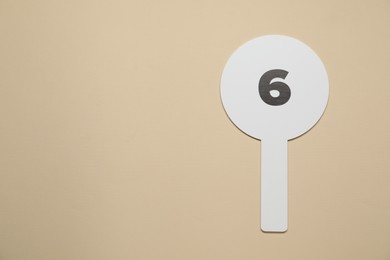 Photo of Auction paddle with number 6 on beige background, top view. Space for text