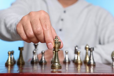Photo of Man moving queen chess piece on checkerboard against light blue background, closeup