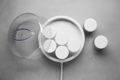 Modern yogurt maker with jars on light grey table, flat lay