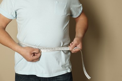 Photo of Man measuring waist with tape on beige background, closeup