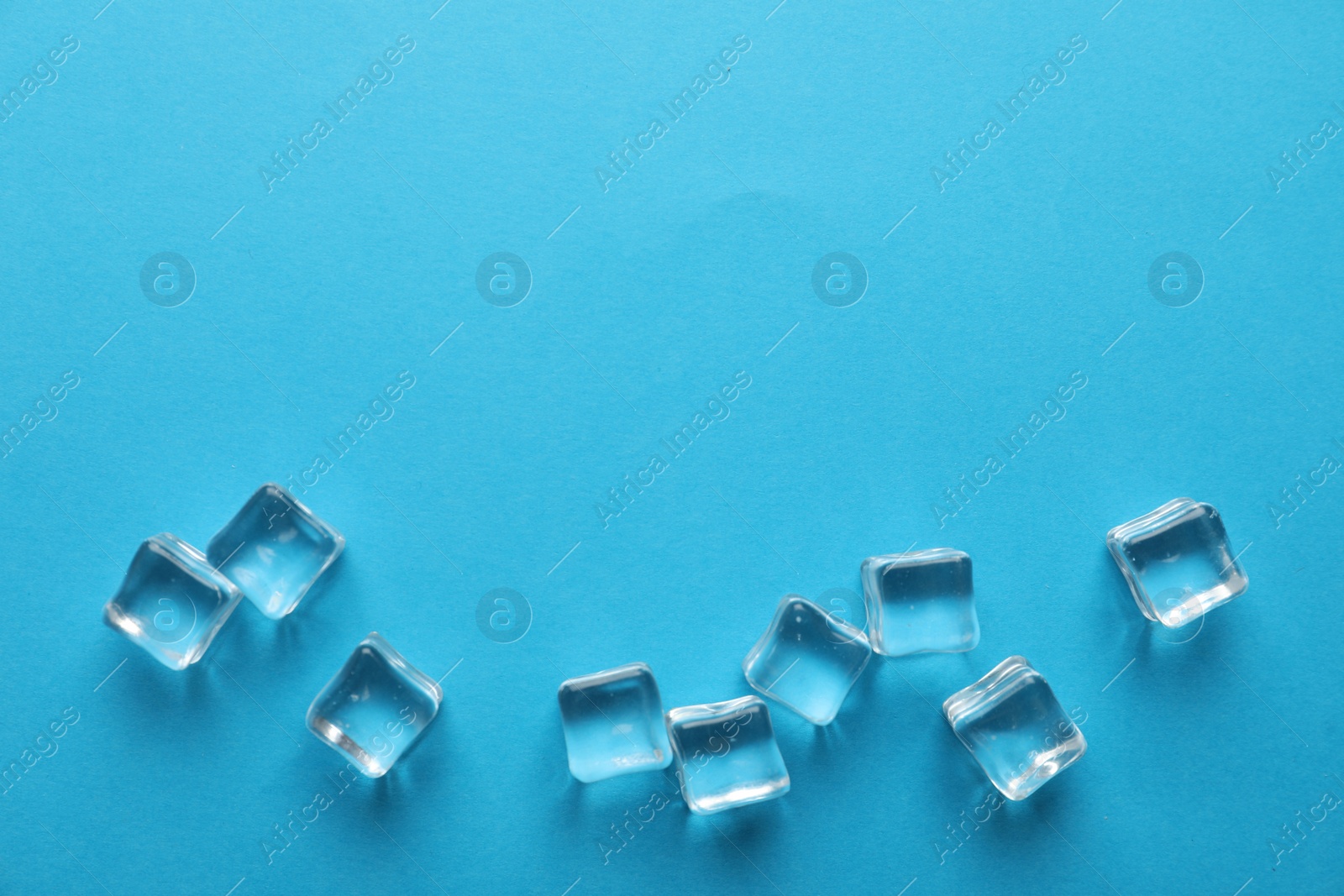 Photo of Crystal clear ice cubes on blue background, flat lay. Space for text