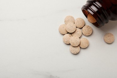 Photo of Overturned bottle with dietary supplement pills on white table, flat lay. Space for text
