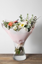 Bouquet of beautiful flowers in vase on wooden table against white wall