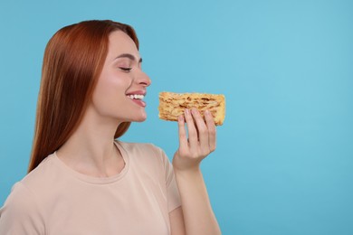 Young woman with tasty cake on light blue background, space for text