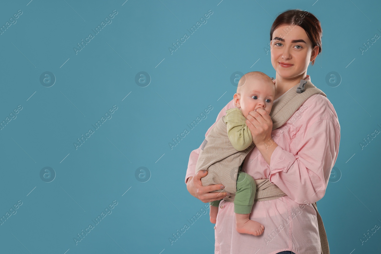 Photo of Mother holding her child in sling (baby carrier) on light blue background. Space for text